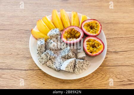 Passionsfrucht, Drachenfrucht, in Scheiben geschnittene Äpfel und schön in einer verzehrfertigen Reisschale auf einem Holztisch angeordnet Stockfoto