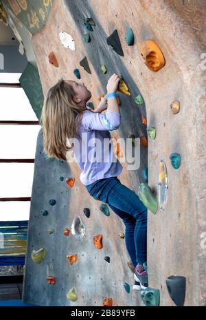 Ein aktives kleines Mädchen klettert an einem Spielort eines Kindes auf eine Felswand in der Halle Stockfoto