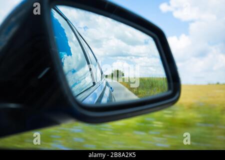 Seitenrückspiegel Fahrzeug spiegelt kurvenreiche Straße in Wald oder Landschaft wider. Dramatische Landschaft Stockfoto