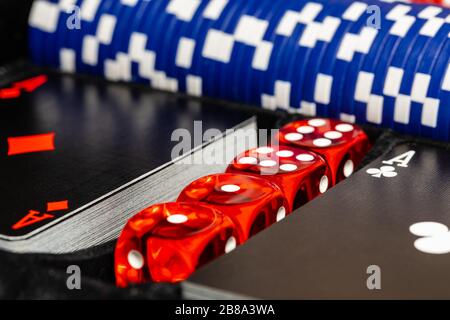 Ein Makro aus zwei einzigartigen schwarzen Kartendecks mit roten Assen, 4 Würfeln und blauen Wettchips in einem Fall. Die Würfel und Chips sind ein Standardkasino. Stockfoto