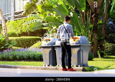 Männer entsorgen Plastikflaschen in Papierkorb, wenn sie seitlich an der Gartenöffentlichkeit, in Mülltonne, in Müll aus Plastikbehältern gehen Stockfoto