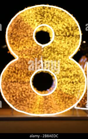 Alphabet Nummer acht Gold, verschwommener Bokeh-Buchstabe acht (8) Goldschriftart bunte Beleuchtung glänzt gelb auf schwarzem Hintergrund in der Nacht Stockfoto