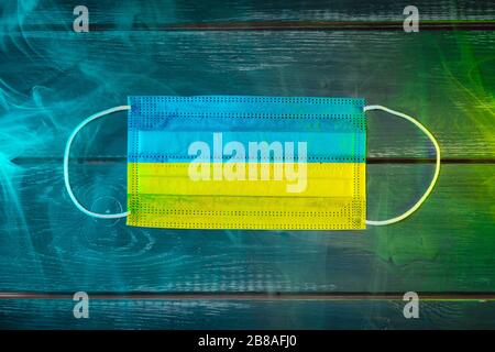 Medizinische Maske zum Schutz vor durch die Luft übertragbaren Krankheiten, in der Nationalflaggen der Ukraine auf schwarzem Grund in blaugrünem Rauch gemalt. Medizinisches Prot Stockfoto