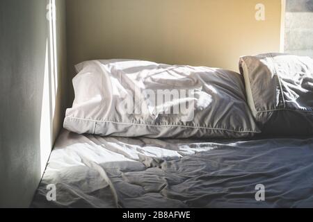 Nahaufnahme der zerknitterten Kissen auf dem zerknitterten Bett in der Nähe der Zimmerecke mit warmem Morgenlicht und Schatten, Kopierbereich Stockfoto