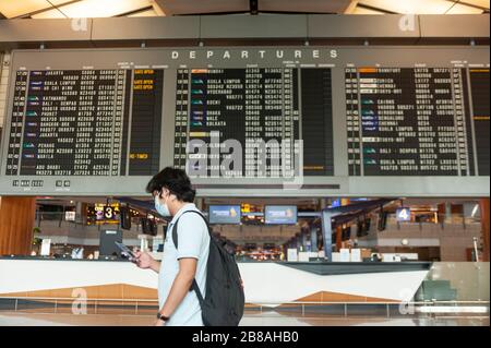 18.03.2020, Singapur, Republik Singapur, Asien - EIN Mann läuft an einer Fluginformationsanzeige in der Abflughalle am Terminal 2 des Flughafens Changi vorbei. Stockfoto