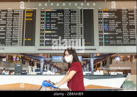 18.03.2020, Singapur, Republik Singapur, Asien - EINE Frau läuft an einer Fluginformationsanzeige in der Abflughalle am Flughafen Changi vorbei. Stockfoto