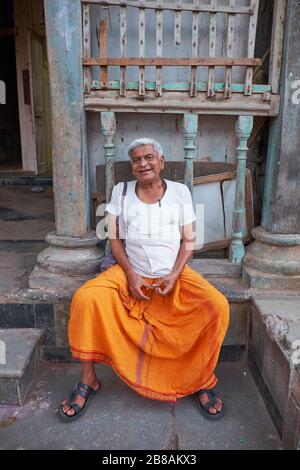 Ein hinduistischer Priester, der mit einem orangefarbenen Dhoti verkleidet ist, entspannt sich außerhalb seiner Residenz in Banganga Tank, einer heiligen Hindu-Pilgerstätte; Walkeshwar, Mumbai, Indien Stockfoto