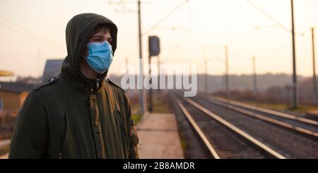 Kerl in einer einmal-medizinischen Maske, die am Bahnhof bei Sonnenuntergang steht. Quarantäne Atemwegserkrankung Epidemie Coronavirus Grippe Public tra Stockfoto