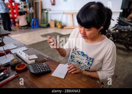 Indonesische Frauen in Asien, die Eigentümerin eines kleinen, örtlichen Familienunternehmens oder lokal Warung genannt werden, berechnen den Gewinn an ihrem Schreibtisch. Selektives Focu Stockfoto