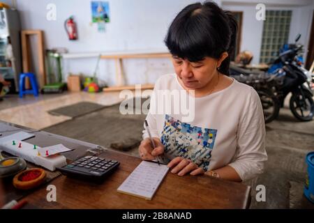 Indonesische Frauen in Asien, die Eigentümerin eines kleinen, örtlichen Familienunternehmens oder lokal Warung genannt werden, berechnen den Gewinn an ihrem Schreibtisch. Selektives Focu Stockfoto