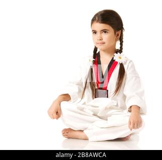 Mädchen in weißem Kimono mit Accessoires in Form von Gänseblümchen auf Schwänzen, in Yoga-Pose auf weißem Hintergrund sitzend und wegschauend Stockfoto