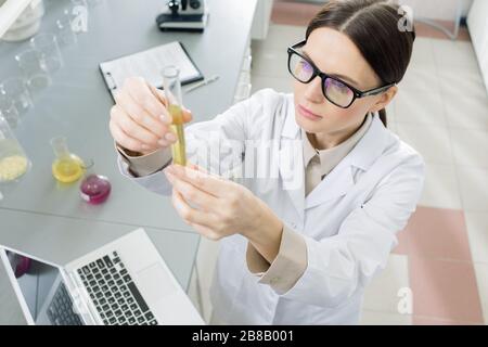 Junge Laborangestellte, die bei der Untersuchung von Coronavirus im Labor mit Flüssigsubstanz auf Kolben blicken, während sie einen neuen Impfstoff untersuchen Stockfoto