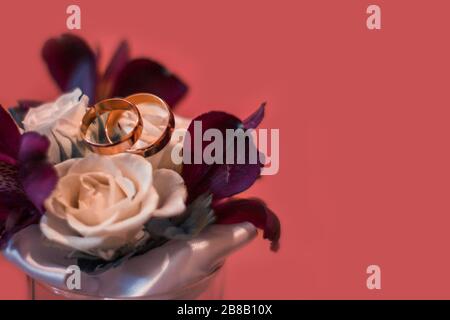 Nahaufnahme der Trauringe auf einem Blumenstrauß unter den Lichtern Vor einem rosa Hintergrund Stockfoto