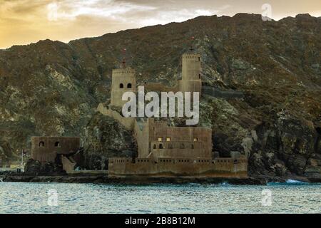 Al Mirani Fort mit Bergen im Hintergrund und Wasserfront beim Sonnenuntergang Stockfoto