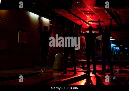 Eine Gruppe junger Freunde mit ihren Armen brachte Freude und Zufriedenheit mit dem Freizeitspiel im Bowlingcenter zum Ausdruck Stockfoto