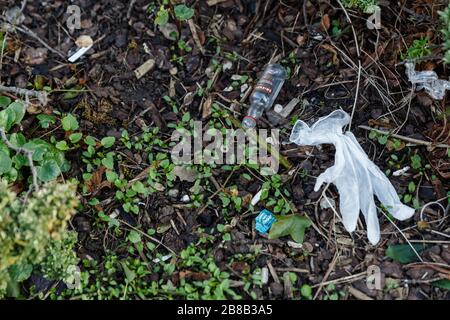 Middlesex, Großbritannien. März 2020. Ein ausrangierter Gummihandschuh und eine leere Miniatur-Wodka-Flasche sitzen unter anderem in einem lokalen Park herum. Menschen tragen Gummihandschuhe, um sich vor dem Coronavirus COVID-19 zu schützen. Mit der Ausbreitung der Pandemie sind Händededesinfektionsmittel sowie andere wichtige Dinge wie toilettenpapier und nicht verderbliche Lebensmittel seit Wochen in Supermärkten ausverkauft. Die Menschen haben nach Alternativen für die Heimwerker-Handwäsche gesucht und da Isopropylalkohol inzwischen auch ausverkauft ist, schlagen soziale Medien Wodka als Ersatz vor. Gutschrift: amanda Rose/Alamy Live News Stockfoto