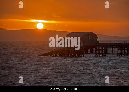 Swansea, Großbritannien, 21. März 2020. Die Sonne geht heute Morgen über die Rettungsstation RNLI im kleinen Dorf Mumbles in der Nähe von Swansea auf, als ein kalter, östlicher Wind über die Swansea Bay weht. Credit: Phil Rees/Alamy Live News Stockfoto