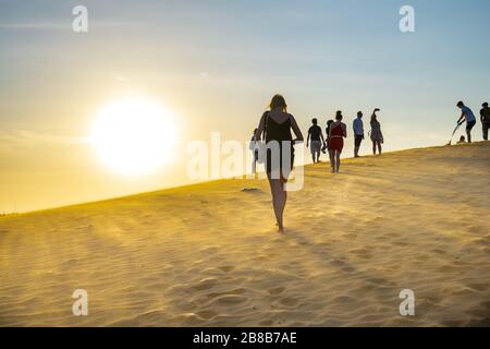 Ausländische Touristen erleben den hohen goldenen Sandhügel, um den Sonnenuntergang über der Wüste im Sommer in Mui Ne, Vietnam, zu beobachten Stockfoto