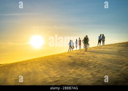 Ausländische Touristen erleben den hohen goldenen Sandhügel, um den Sonnenuntergang über der Wüste im Sommer in Mui Ne, Vietnam, zu beobachten Stockfoto