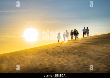 Ausländische Touristen erleben den hohen goldenen Sandhügel, um den Sonnenuntergang über der Wüste im Sommer in Mui Ne, Vietnam, zu beobachten Stockfoto