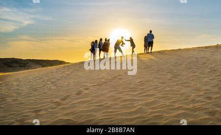 Ausländische Touristen erleben den hohen goldenen Sandhügel, um den Sonnenuntergang über der Wüste im Sommer in Mui Ne, Vietnam, zu beobachten Stockfoto