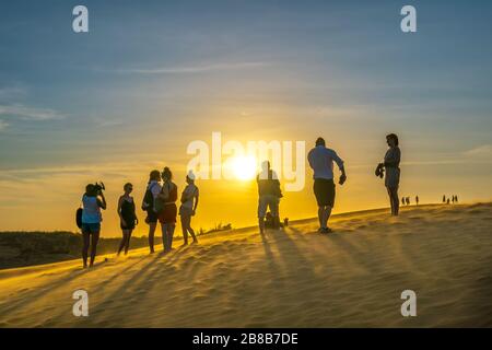 Ausländische Touristen erleben den hohen goldenen Sandhügel, um den Sonnenuntergang über der Wüste im Sommer in Mui Ne, Vietnam, zu beobachten Stockfoto