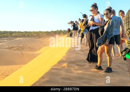 Ausländische Touristen erleben den hohen goldenen Sandhügel, um den Sonnenuntergang über der Wüste im Sommer in Mui Ne, Vietnam, zu beobachten Stockfoto