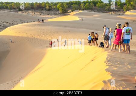 Ausländische Touristen erleben den hohen goldenen Sandhügel, um den Sonnenuntergang über der Wüste im Sommer in Mui Ne, Vietnam, zu beobachten Stockfoto