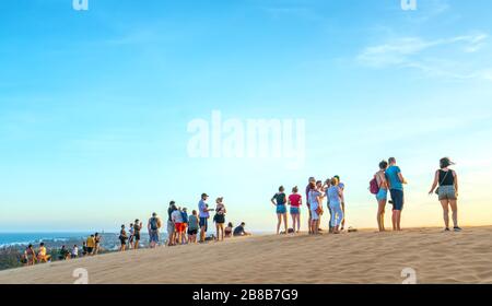 Ausländische Touristen erleben den hohen goldenen Sandhügel, um den Sonnenuntergang über der Wüste im Sommer in Mui Ne, Vietnam, zu beobachten Stockfoto