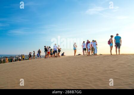 Ausländische Touristen erleben den hohen goldenen Sandhügel, um den Sonnenuntergang über der Wüste im Sommer in Mui Ne, Vietnam, zu beobachten Stockfoto