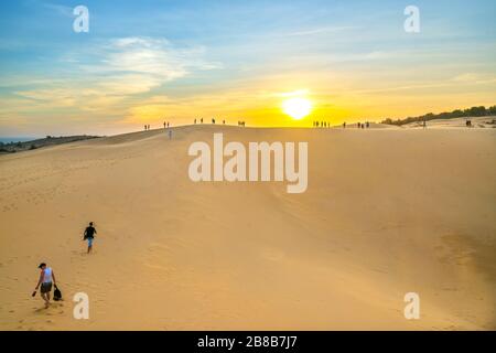 Ausländische Touristen erleben den hohen goldenen Sandhügel, um den Sonnenuntergang über der Wüste im Sommer in Mui Ne, Vietnam, zu beobachten Stockfoto