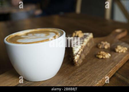 Nahaufnahme mit selektivem Fokus von einem Cappuccino und einem Stück Von Kuchen und Walnüssen auf einer hölzernen Oberfläche Stockfoto