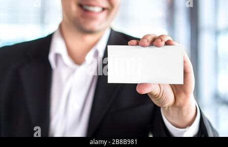 Fröhlicher lächelnder Business man hält leere weiße Visitenkarte im modernen Bürogebäude. Freier leerer Kopierspeicher. Stockfoto
