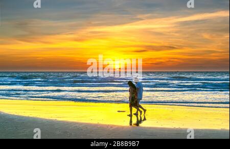Eine Silhouette eines ausländischen Touristenpaares, das gerne an einem weißen Sandstrand entlang spazieren geht, wenn der Sonnenaufgang in Mui Ne, Vietnam friedlich ist Stockfoto