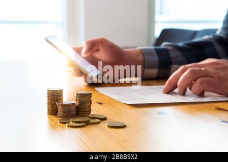 Bezahlen elektronischer Rechnungen mit Smartphone. Digitale Internet-Zahlung mit Handy. Mann mit Handy und Online-Bank. Lesen von Papier und Tippen. Stockfoto