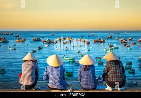 Eine Gruppe vietnamesischer Frauen, die am frühen Morgen in einem kleinen Dorf in der Nähe von Mui Ne, Vietnam, auf das Fischerboot am Hafen warten. Stockfoto