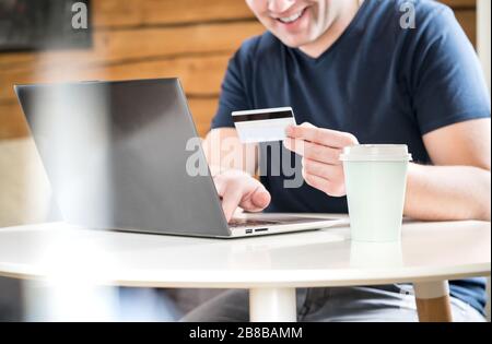 Glücklicher Mann, der mit Kreditkarte bezahlt oder eine Online-Bank mit Laptop verwendet. Fröhlicher und lächelnder Typ, der Informationen oder Zahlen auf den Computer schreibt. Stockfoto