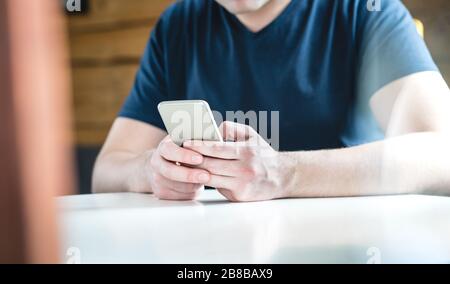 Junger Mann mit Smartphone textet. Kerl mit Handy vor Holzwand und Hintergrund. Nahaufnahme der Hände, die das Handy halten. Stockfoto