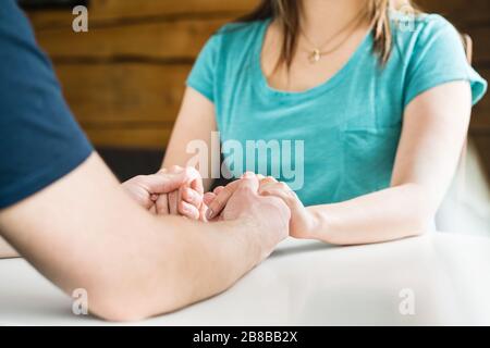 Paar, die Hände am Tisch zusammenhalten. Unterstützung, Hilfe, Fürsorge, Vergebung oder Entschuldigung. Mann tröstet traurige Frau. Mitgefühl und Einfühlungsvermögen. Stockfoto