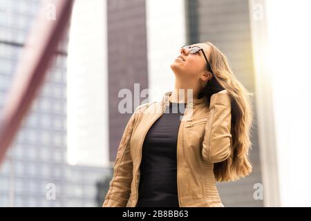 Selbstbewusste Brunette-Frau, die in der Stadt spazieren geht. Starke Dame, die bei Sonnenuntergang braune Haare feilte. Urbaner modischer Lebensstil. Stockfoto