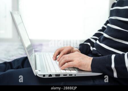 Ein Mann mittleren Alters, der sich zu Hause beiläufig anzog und mit einem Computer von zu Hause aus arbeitet. Stockfoto