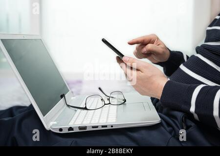 Ein Mann mittleren Alters, der sich zu Hause beiläufig anzog und mit einem Computer von zu Hause aus arbeitet. Stockfoto