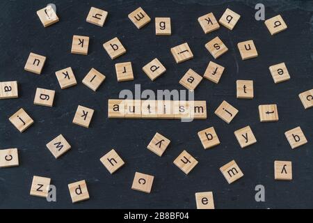 Autismus buchstabierte in Holzklötze mit Buchstaben, die zufällig um das Bild auf dunklem Schieferhintergrund verteilt waren. Stockfoto