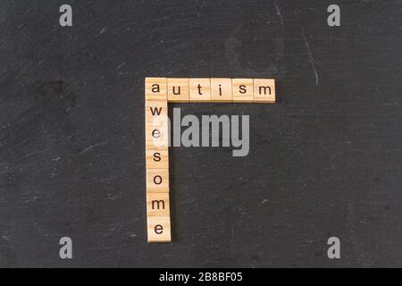 Autismus und Awesome stachelten in Holzbuchstabenblocks auf dunklem Schiefergrund. Copyspace. Stockfoto