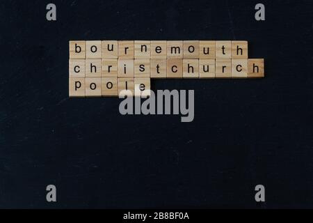Bournemouth Christchurch Poole buchstabierte in Holzblöcken auf dunklem Schiefergrund. Copyspace unten, Querformat Stockfoto