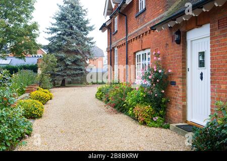 Englisches Landhaus und Garten im Herbst mit einer Schottereinfahrt. Das Haus ist viktorianisch, mit Blumenrändern, die mit Sträuchern und mehrjährigen Pflanzen gefüllt sind Stockfoto