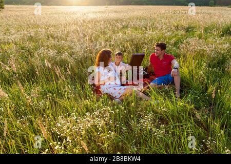 Eine glückliche Familie verbringt Zeit in der Natur. Sie sitzen an einem sonnigen Sommertag auf der Decke auf dem Feld.schwangere Familienfotos in der Natur Stockfoto