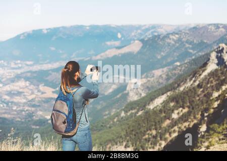 Tourist Mädchen, die ein Fotoshooting von Berg machen. Das junge, schöne Mädchen reist allein im Frühjahr oder Herbst in die Berge, blickt in die Ferne und genießt Natur, Felsen und grüne Wälder, Blick auf die Landschaft, einen Rucksack dahinter und Sportswear, Freiheit und Leichtigkeit. Stockfoto