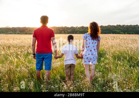 Ein Ehemann, seine Frau und ein junger Sohn posieren bei Sonnenuntergang auf dem Weizenfeld.schwangere Familienfotos schießen in der Natur Stockfoto