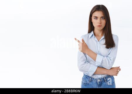 Beleidigt schwült süßes kaukasisches Mädchen in blauer Bluse, die mit dem Finger nach links zeigt, peitscht und mit beleidigtem Jammern oder beschwerlichem Ausdruck Kamera sieht Stockfoto